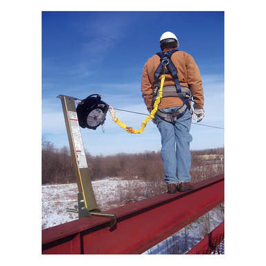 A person confidently stands on a red steel beam, clad in safety gear and a helmet, secured by the 3M DBI-SALA EZ-Line Retractable Horizontal Lifeline System. The winter landscape, adorned with snow-dusted trees, provides the backdrop for this demonstration of user-friendly installation and enhanced worker satisfaction offered by 3M DBI-SALA Fall Protection.