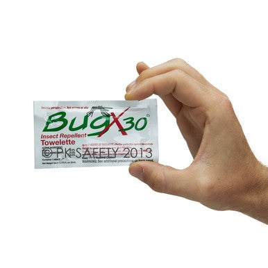 A hand holds a small packet labeled "Coretex BugX30 Insect Repellent Towelette with Deet," featuring additional text that includes "PK Safety 2013," against a white background.