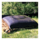 An UltraTech Dewatering Bag 972_-OS (black, large) sits on grass with a hose attached, surrounded by hay bales. Lush green trees and shrubs in the background show effective stormwater pollution prevention by UltraTech.