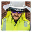 A construction worker wearing an NSA-branded white hard hat equipped with the DRIFIRE Hard Hat Sunshade Kit (KITDFSUNSHD), reflective sunglasses, and a neon yellow high-visibility vest stands in front of a brick wall.