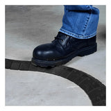 A person wearing dark blue jeans and black work boots stands on the UltraTech Black Sidewinder System with Endcaps 1802 by UltraTech International, effectively safeguarding against tripping hazards on the concrete surface.