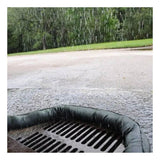Rainwater flows into a street storm drain, shielded by UltraTech International's UltraTech Filter Sock, which acts as a protective barrier to block debris and efficiently remove pollutants. The road and nearby grass, soaked from the rainfall, benefit from the advanced stormwater protection provided by this setup.