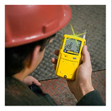A person in a red hard hat holds a BW XT-XWHM-Y-NA Honeywell GasAlert Max XT II by BW Technologies, using the multi-gas monitor’s digital display and flashing light to check air quality on an industrial floor.