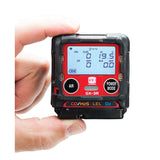 A hand holds an RKI Instruments GX-3R 4 Gas Confined Space Monitor 72-RA-C, displaying CO, H2S, LEL, and O2 levels with visible "AIR" and "POWER MODE" buttons—a reliable monitor for confined spaces.
