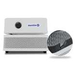 The Austin Air Systems "it" Machine C100 is a compact white air purifier with a control knob and perforated front panel, shown with an inset highlighting its internal filter mesh and layers for effective removal of airborne particles.