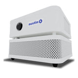 The Austin Air Systems "it" Machine C100 is a compact white rectangular air purifier with a black circular dial, bottom ventilation holes, and four small feet for effective removal of airborne particles.