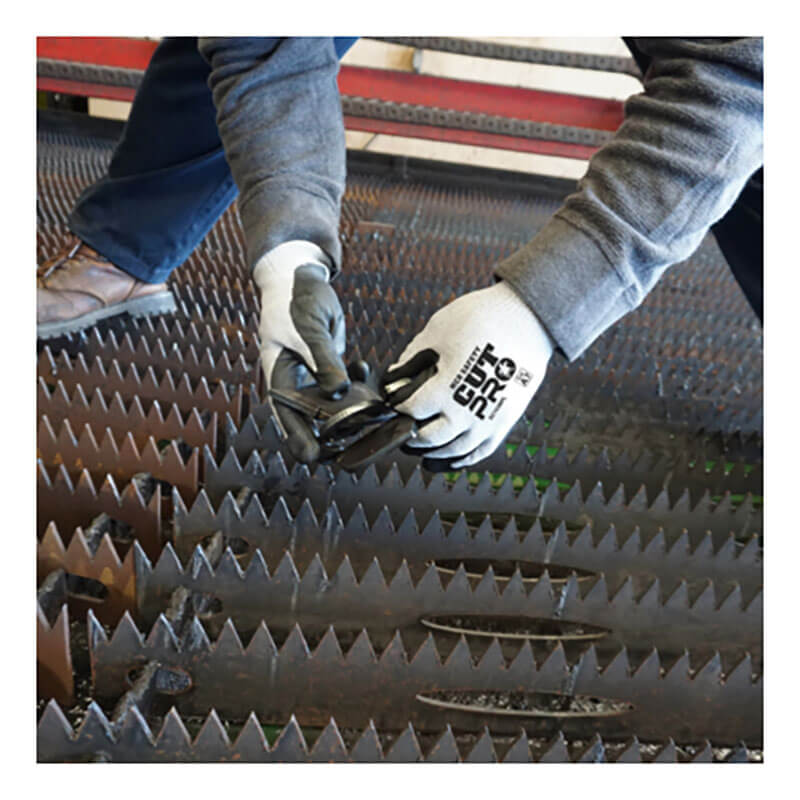 A person wearing MCR Safety Cut Pro 13G HyperMax Bi-polymer Gloves (92743BP) inspects jagged metal, while another person’s feet are seen in the background.