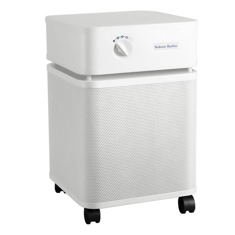 The Austin Air Systems Bedroom Machine B402 is a white, box-shaped air purifier with a top control knob, front ventilation holes, medical-grade HEPA filtration, and four black caster wheels.